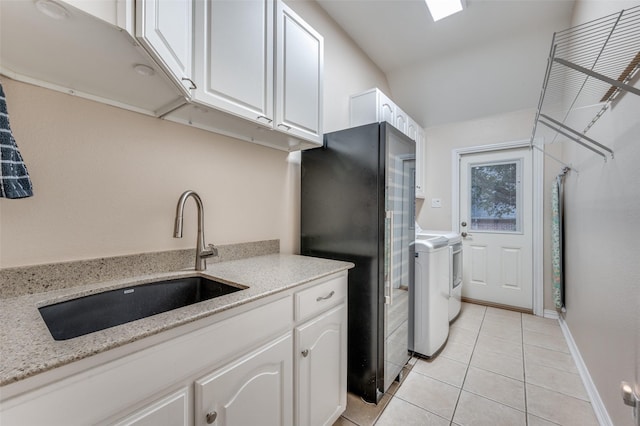 laundry room featuring cabinet space, light tile patterned floors, baseboards, washing machine and dryer, and a sink