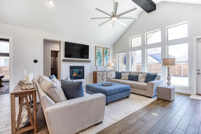 living area with high vaulted ceiling, a glass covered fireplace, beamed ceiling, and wood finished floors