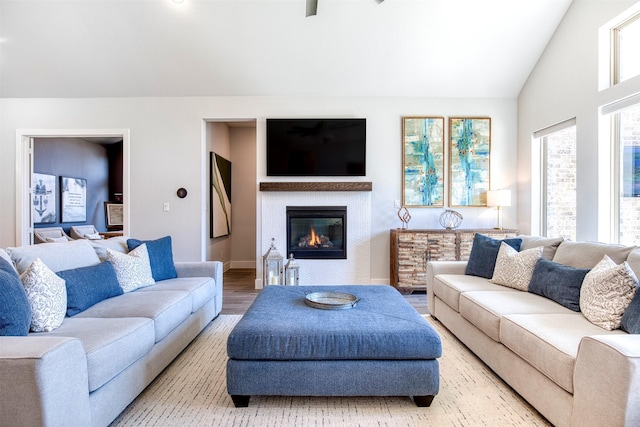 living room with lofted ceiling, a glass covered fireplace, baseboards, and wood finished floors