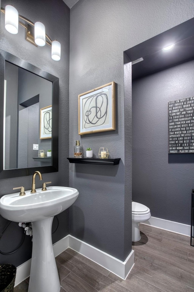 half bath featuring a textured wall, toilet, baseboards, and wood finished floors