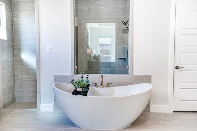 bathroom with a soaking tub, baseboards, and tiled shower