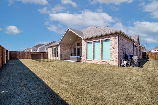 rear view of property with a fenced backyard, brick siding, a shingled roof, an outdoor living space, and a lawn