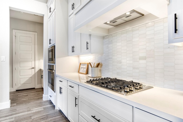 kitchen with custom range hood, appliances with stainless steel finishes, light countertops, light wood-type flooring, and white cabinetry