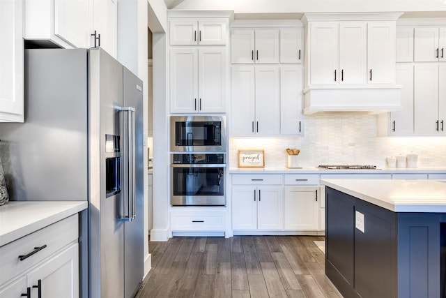 kitchen with premium range hood, wood finished floors, white cabinetry, light countertops, and appliances with stainless steel finishes