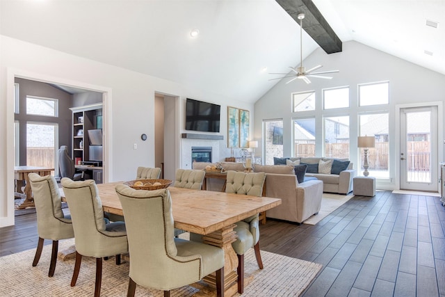 dining room with a glass covered fireplace, dark wood-style floors, ceiling fan, beamed ceiling, and high vaulted ceiling