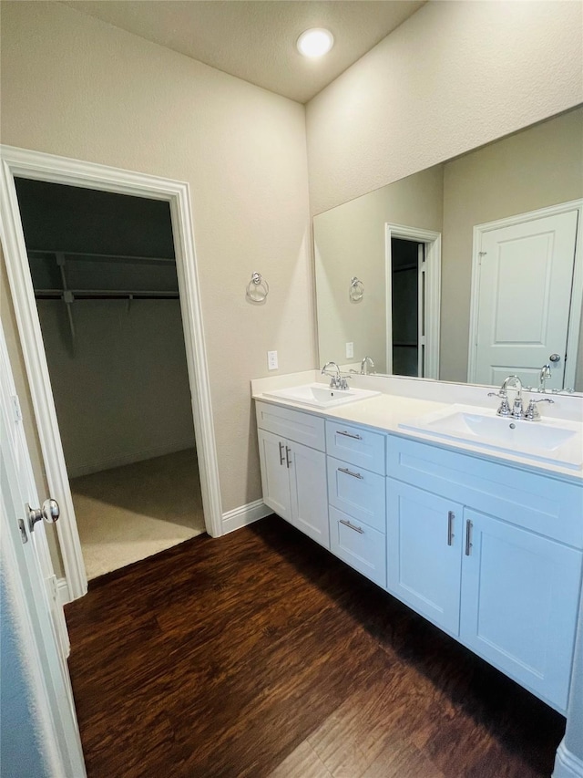 full bath featuring double vanity, wood finished floors, a sink, and a walk in closet