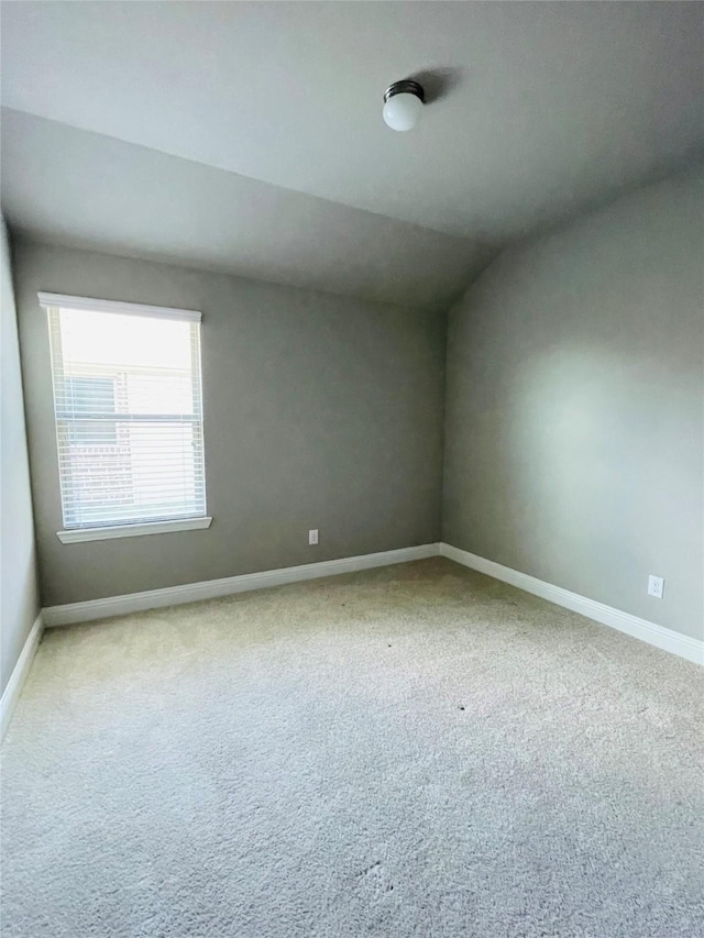 carpeted empty room featuring lofted ceiling and baseboards