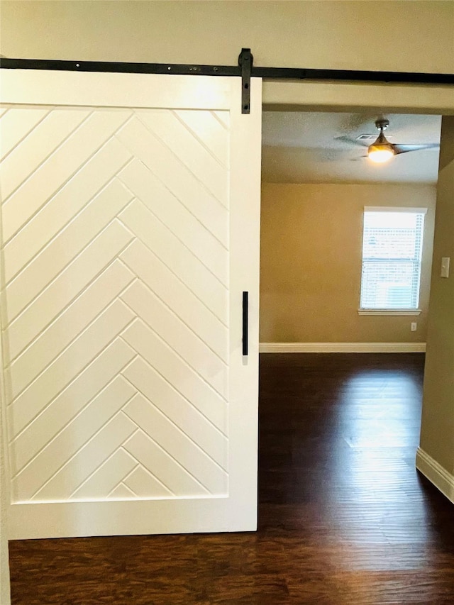 spare room with a barn door, baseboards, and dark wood finished floors