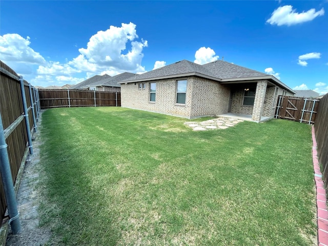 back of property featuring brick siding, a fenced backyard, roof with shingles, and a yard