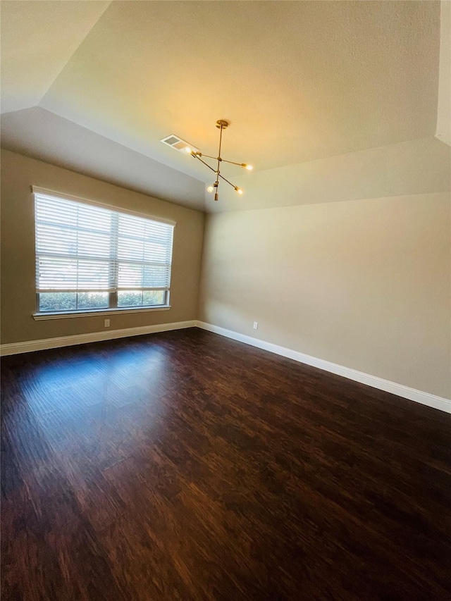 spare room featuring dark wood-type flooring, lofted ceiling, baseboards, and an inviting chandelier