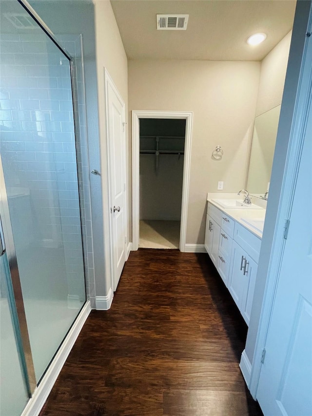 full bath featuring a walk in closet, double vanity, a stall shower, a sink, and wood finished floors