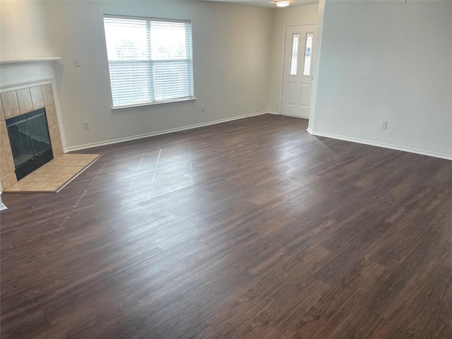 unfurnished living room featuring baseboards, dark wood finished floors, and a tile fireplace