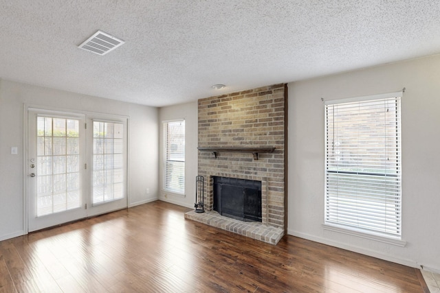 unfurnished living room featuring visible vents, a fireplace, a textured ceiling, and wood finished floors