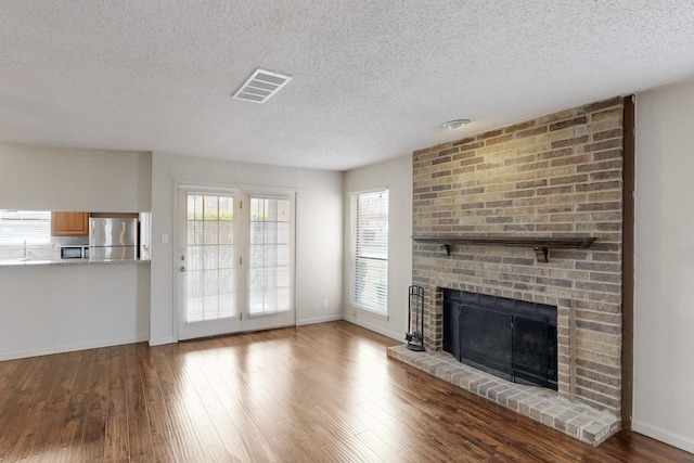 unfurnished living room featuring visible vents, a fireplace, baseboards, and wood finished floors