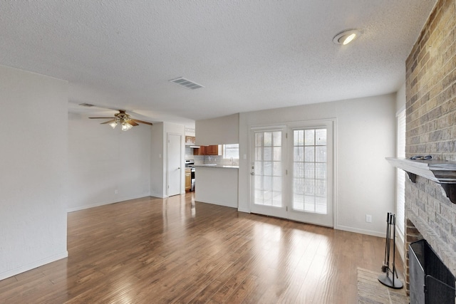 unfurnished living room with a fireplace, visible vents, a ceiling fan, a textured ceiling, and wood finished floors