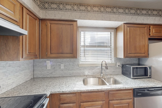 kitchen with appliances with stainless steel finishes, brown cabinets, a sink, and under cabinet range hood