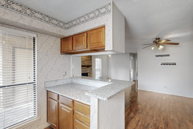 kitchen with a ceiling fan, wood finished floors, a peninsula, a textured ceiling, and a fireplace