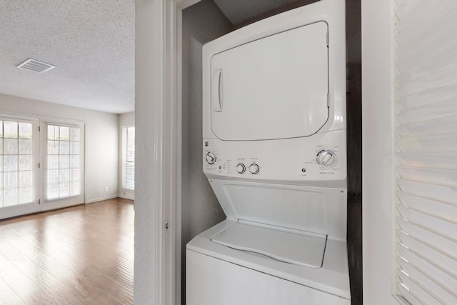 laundry room featuring a textured ceiling, laundry area, wood finished floors, visible vents, and stacked washing maching and dryer