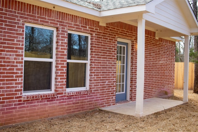 doorway to property featuring roof with shingles and brick siding