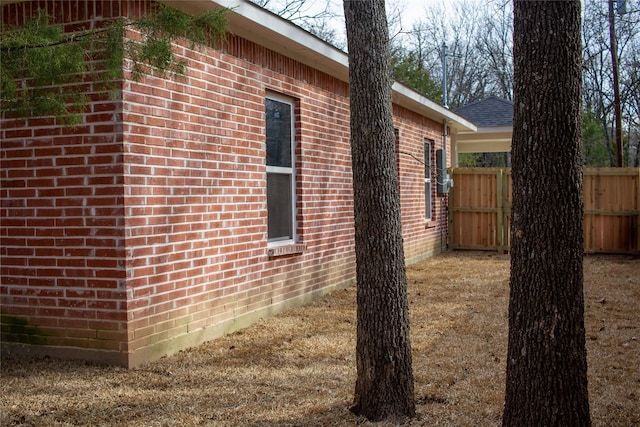 view of property exterior featuring roof with shingles, fence, and brick siding