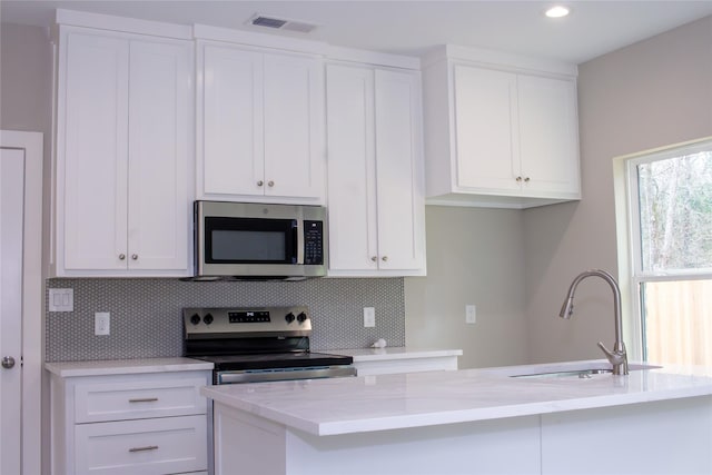 kitchen with stainless steel appliances, white cabinetry, a sink, and backsplash