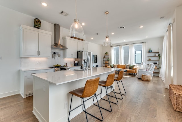 kitchen with visible vents, wall chimney range hood, a sink, and appliances with stainless steel finishes