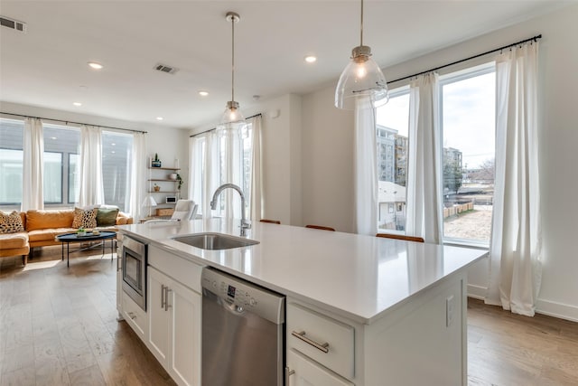 kitchen featuring visible vents, open floor plan, stainless steel appliances, light wood-type flooring, and a sink