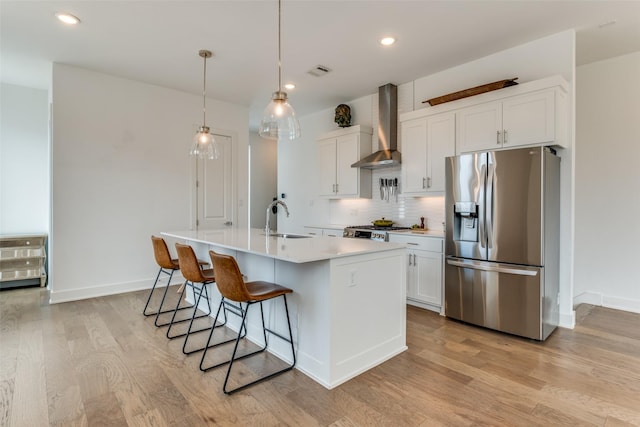 kitchen with light wood-style floors, backsplash, wall chimney range hood, stainless steel refrigerator with ice dispenser, and a sink