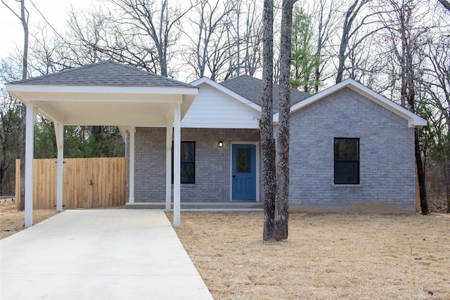 view of front facade with concrete driveway, brick siding, roof with shingles, and fence