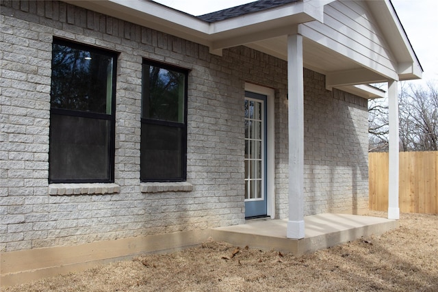 view of property exterior featuring a shingled roof, fence, and brick siding