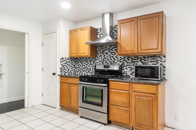 kitchen featuring light tile patterned floors, stainless steel range with gas stovetop, dark stone countertops, wall chimney range hood, and backsplash