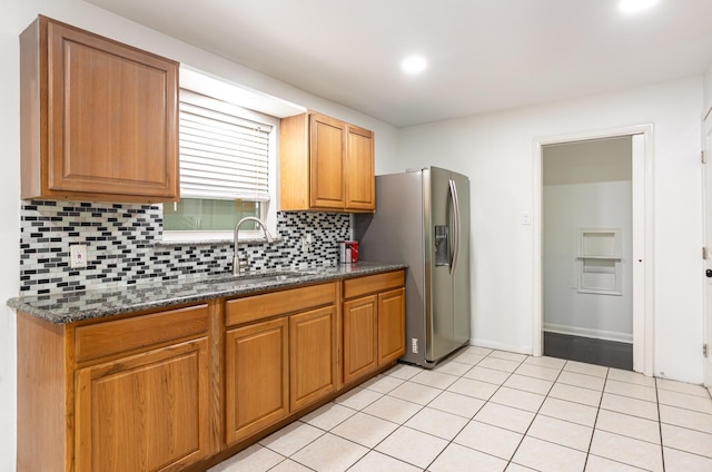 kitchen featuring light tile patterned flooring, a sink, backsplash, brown cabinets, and stainless steel fridge