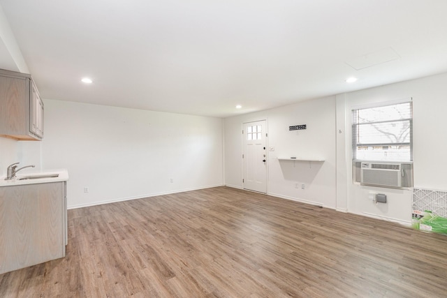 unfurnished living room with cooling unit, recessed lighting, a sink, baseboards, and light wood finished floors