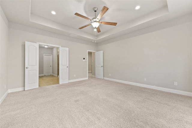 unfurnished bedroom with recessed lighting, light carpet, a raised ceiling, and baseboards
