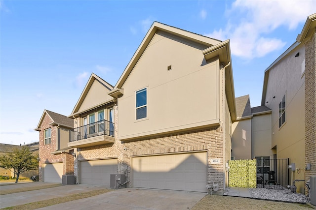 view of front of house with a garage, brick siding, central AC, and stucco siding