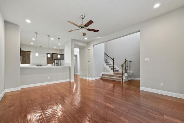 unfurnished living room featuring stairs, wood finished floors, a ceiling fan, and baseboards