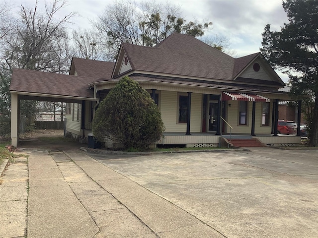 farmhouse-style home with covered porch, driveway, a carport, and roof with shingles