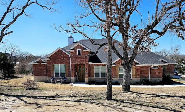 view of front of property featuring roof with shingles, a chimney, and brick siding