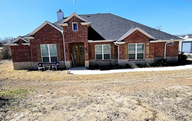 view of front of house featuring french doors, brick siding, a chimney, and roof with shingles