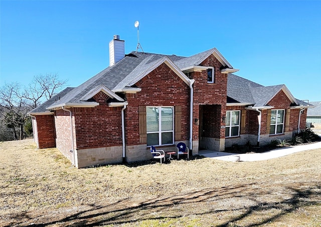 view of front of house featuring roof with shingles, brick siding, and a chimney