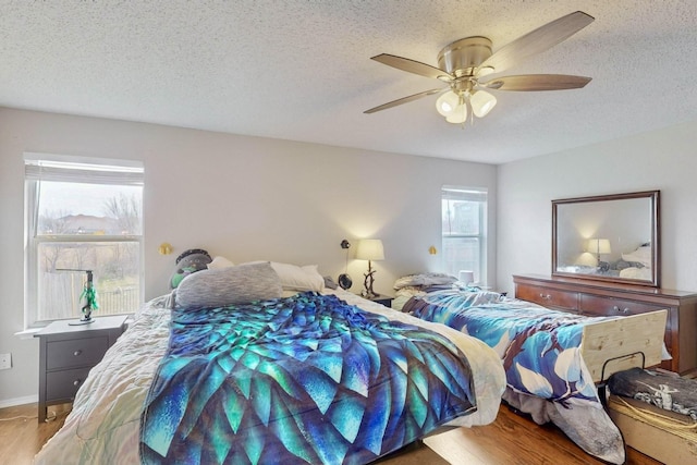 bedroom with a ceiling fan, a textured ceiling, baseboards, and wood finished floors