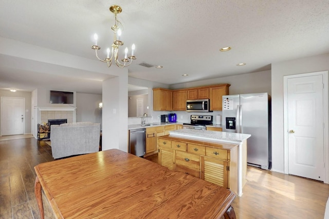 kitchen featuring stainless steel appliances, a kitchen island, a sink, light countertops, and a tiled fireplace