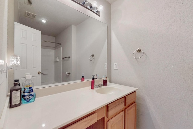 full bathroom with visible vents, a textured wall, vanity, and walk in shower