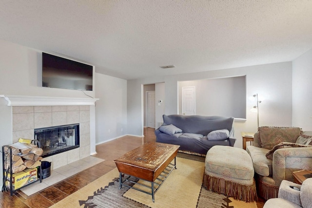 living room featuring baseboards, visible vents, wood finished floors, a textured ceiling, and a fireplace