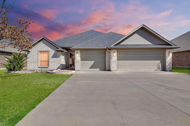 view of front of home featuring driveway, an attached garage, a shingled roof, a front lawn, and brick siding