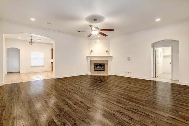 unfurnished living room featuring baseboards, a tile fireplace, ceiling fan, wood finished floors, and crown molding