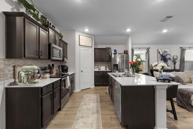 kitchen with visible vents, appliances with stainless steel finishes, open floor plan, a sink, and dark brown cabinets