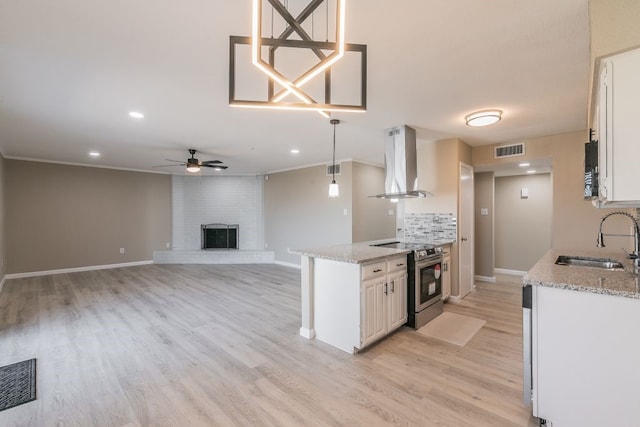 kitchen featuring wall chimney range hood, a sink, visible vents, and stainless steel range with electric cooktop