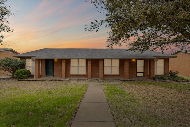 ranch-style house featuring roof with shingles, brick siding, and a front lawn