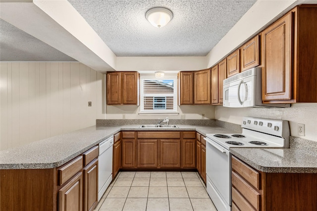 kitchen featuring light tile patterned floors, a peninsula, white appliances, a sink, and brown cabinetry